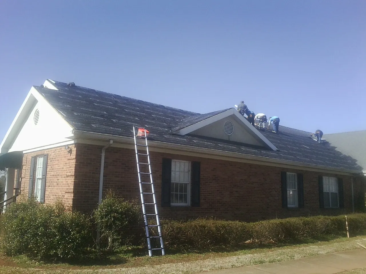 Crew tearing shingles off a brick ranch roof with a ladder set — Metal Roof Repair work by our crew in Monroeville