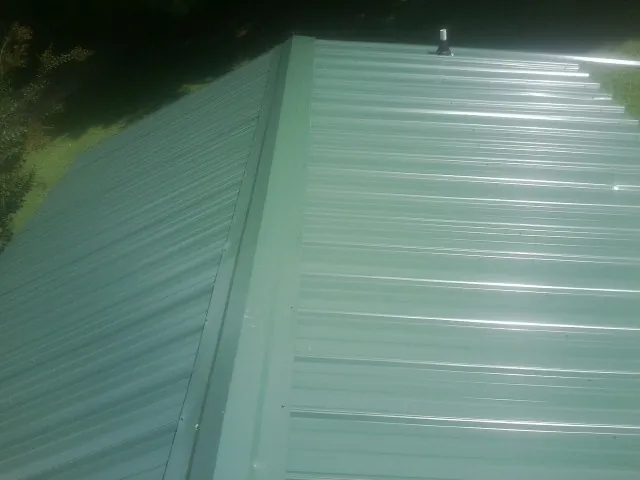 New green metal panels meeting at the ridge of a roof — Flat Roof Repair work by our crew in Monroeville