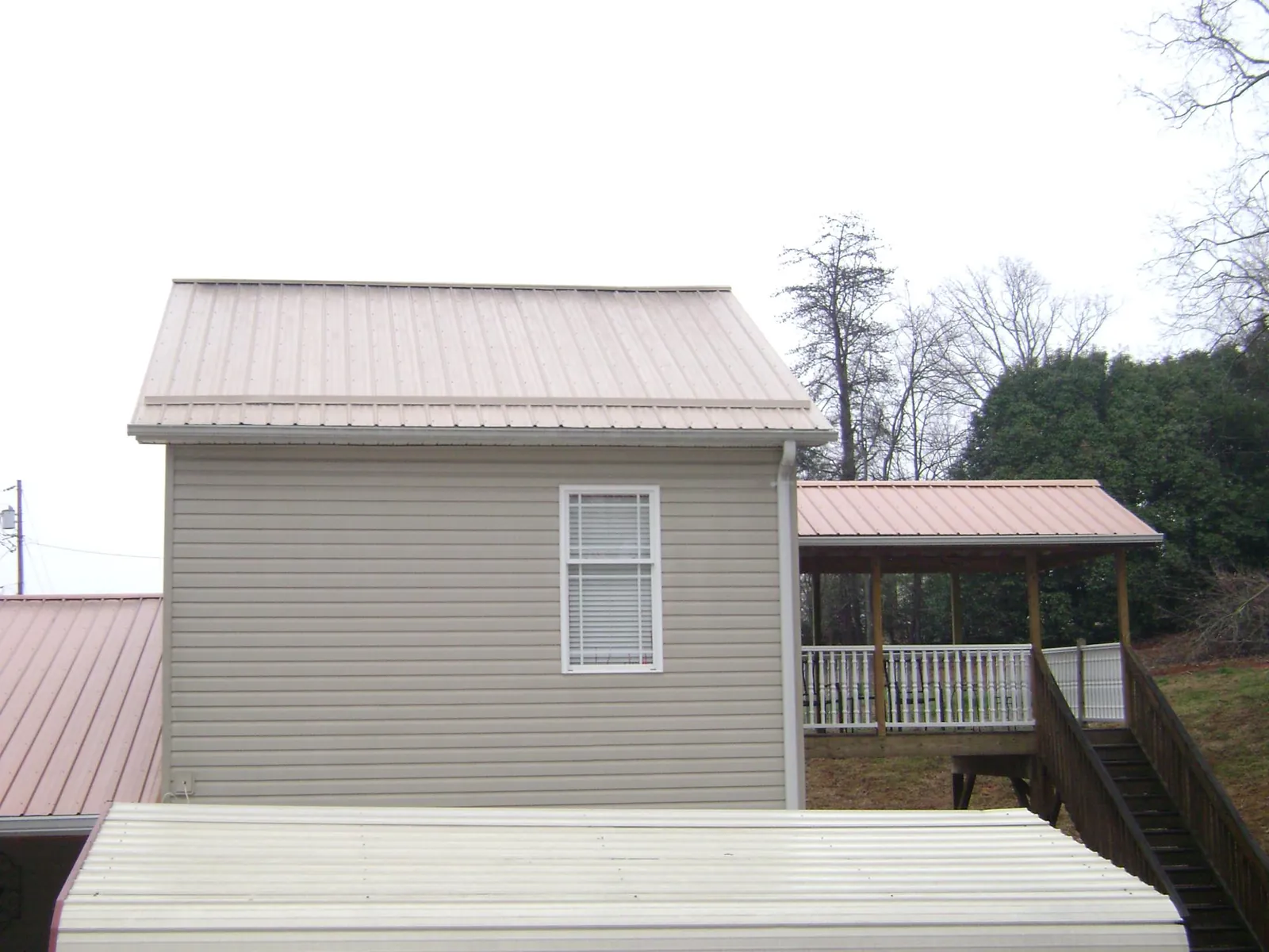 Tan metal roofs on a two story addition and attached porch, from a Roof Replacement job in Monroeville